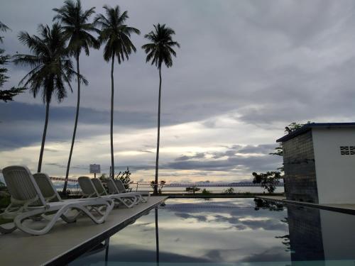 a pool with chairs and palm trees in the background at Rafflesia Resort in Lundu