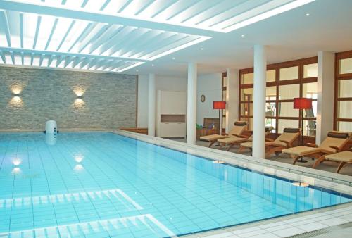 a pool in a hotel with chairs and a room at Bio Thermalhotel Falkenhof in Bad Füssing