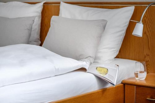 a bed with white pillows and a book and a glass of wine at Hotel Maier in Friedrichshafen