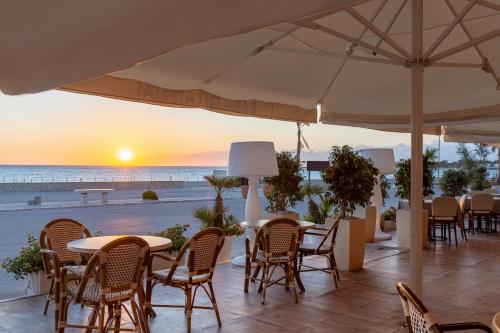 a patio with tables and chairs and the beach at sunset at Mira Spiaggia in San Vito lo Capo