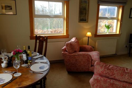 sala de estar con mesa, sillas y 2 ventanas en Blairchroisk Cottage en Pitlochry
