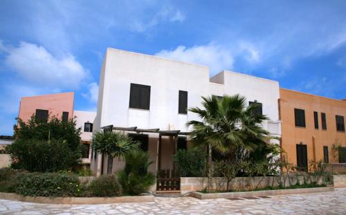 a white building with a palm tree in front of it at Residence Favonio in Favignana