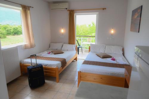 two beds in a room with a window and a suitcase at Hotel Geromichalos in Paralía Skotínis