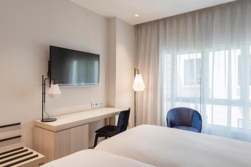 a hotel room with a bed and a desk and a tv at Eurostars Mediterranea Plaza in Alicante