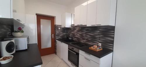 uma cozinha com armários brancos e um balcão preto em Apartment Lukrecija em Selce