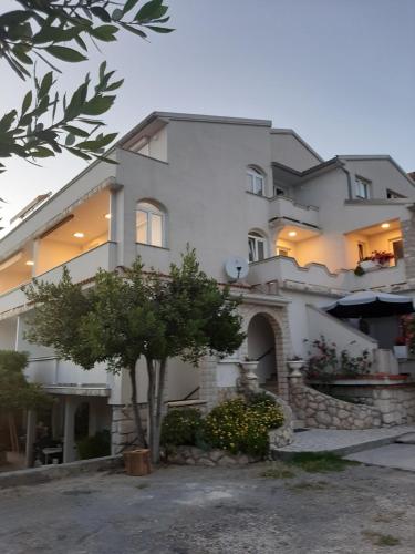 un gran edificio blanco con un árbol delante en Apartmans and rooms Petra, en Rab