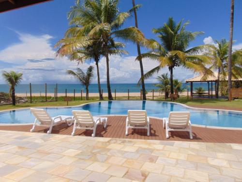 uma piscina com cadeiras e palmeiras e o oceano em Areias de Itacimirim em Itacimirim