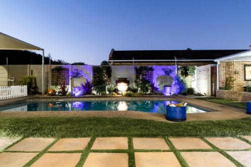 una piscina en el patio trasero por la noche con luces púrpuras en Wagtails Guest House, en Port Elizabeth