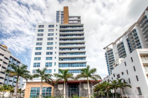 a tall white building with palm trees in front of it at Bluebird Suites Monte Carlo Miami Beach in Miami Beach