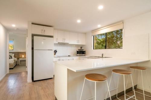 a kitchen with white cabinets and a counter with stools at Gosamara Apartments in Byron Bay