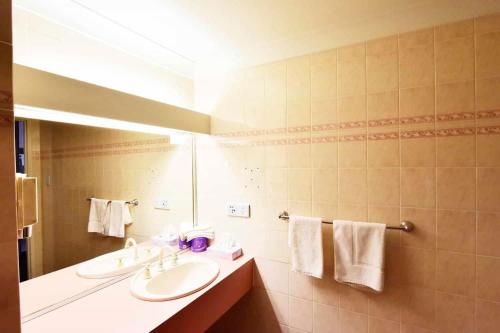 a bathroom with two sinks and a mirror and towels at Diplomat Hotel Alice Springs in Alice Springs