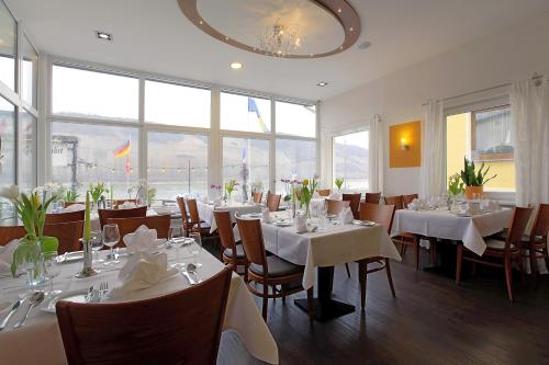 ein Restaurant mit weißen Tischen, Stühlen und Fenstern in der Unterkunft Lindenhof in Osterspai