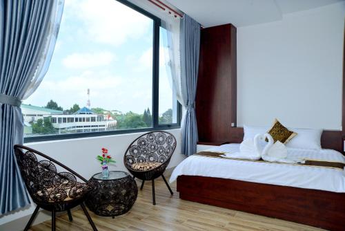 a bedroom with a bed and two chairs and a large window at Buon Ma Thuot Hotel in Buon Ma Thuot