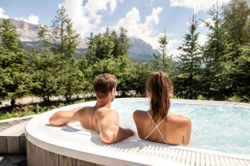 a man and woman sitting on a surfboard in a pool at Hotel Lech Da Sompunt in Badia