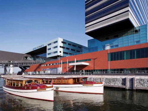zwei Boote im Wasser vor einem Gebäude in der Unterkunft Mövenpick Hotel Amsterdam City Centre in Amsterdam
