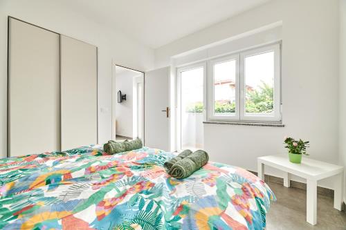 a white bedroom with a colorful bed and windows at Apartmani Ivana in Umag