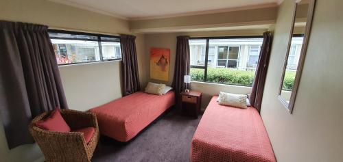 a room with two beds and two chairs and windows at Accent On Taupo Motor Lodge in Taupo