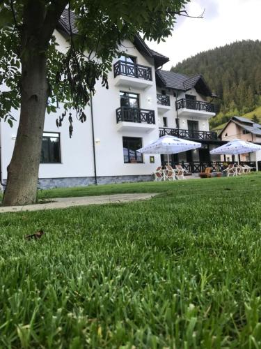 a large white building with people sitting under umbrellas at Pensiunea Edelweiss in Voineasa