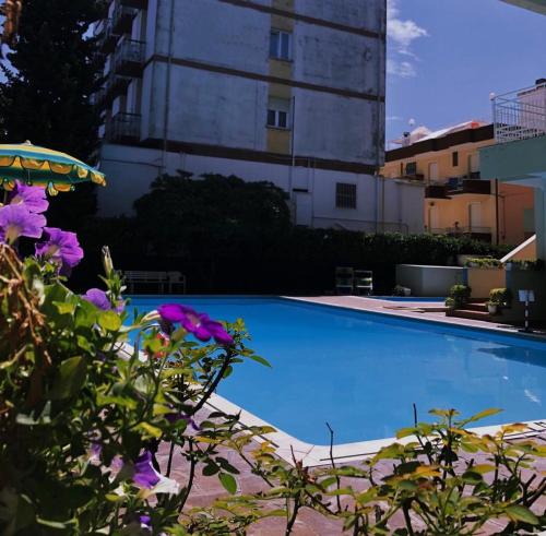 una piscina con flores púrpuras frente a un edificio en Hotel Susy en Rímini