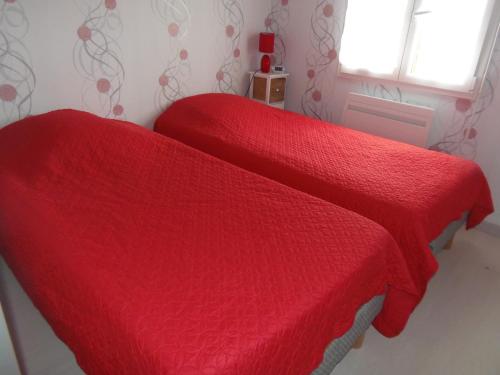 two beds with red covers in a room with a window at petite maison de vacance in Grandcamp-Maisy