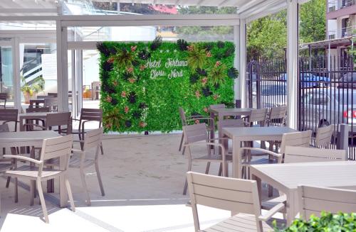 een restaurant met witte tafels en stoelen en een groene haag bij Hotel Fortuna in Eforie Nord