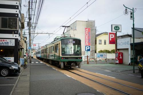 a green train traveling down the tracks in a city at Trawl Guesthouse トロールゲストハウス Breakfast Options in Koshigoe