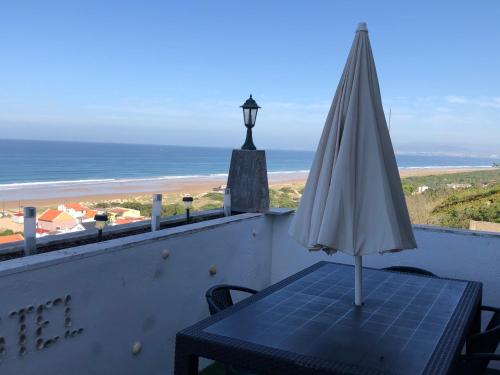 a table with an umbrella on a balcony with the beach at Fonte da Telha Beach Hostel in Costa da Caparica