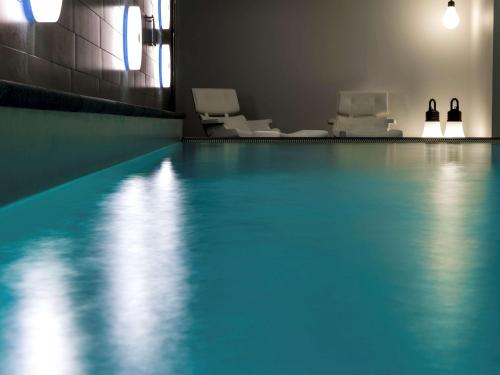 a swimming pool with white chairs in a room at Pullman Eindhoven Cocagne in Eindhoven