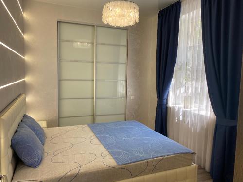 a bedroom with a bed with blue curtains and a chandelier at New luxury Apartment in the Center on Konstitution Square in Kharkiv