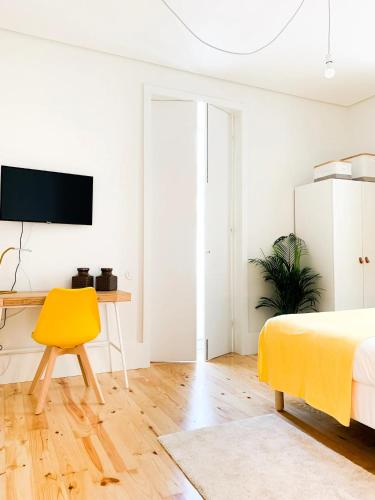 a white bedroom with a yellow chair and a desk at Guest House Arca de Água in Porto