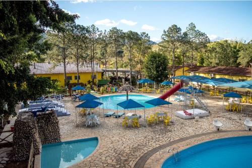 un complejo con una piscina con mesas y sombrillas en Hotel Fazenda Pé da Serra, en Bom Sucesso