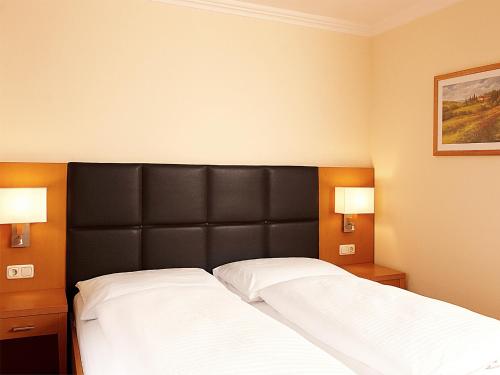 a bedroom with a bed with a black headboard and two lights at Hotel Goldener Adler in Linz