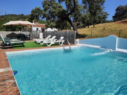 una gran piscina con sillas y una mesa en CASA RURAL LA DEHESILLA, en Cazalla de la Sierra