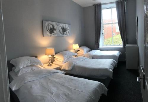 a group of four beds in a room with a window at The Station Apartment in Kilmarnock