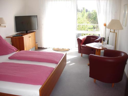 a bedroom with a bed and chairs and a television at Hotel Kurallee in Meersburg