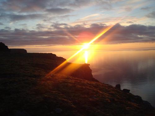 a person is standing on a cliff watching the sunset at Hænuvík Cottages in Örlygshöfn
