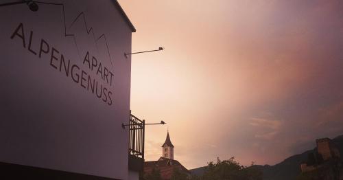 a building with a clock tower with the sunset in the background at Apart Alpengenuss in Ladis