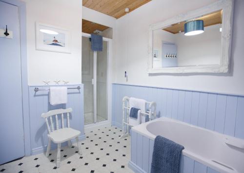 Margaret's Cottage B&B في Ardglass: حمام باللون الأزرق والأبيض مع حوض استحمام وكرسي