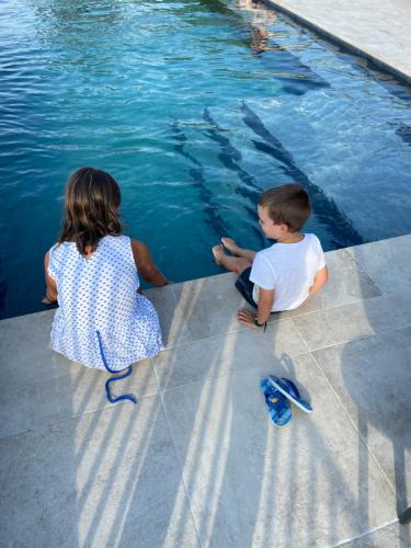 two children sitting on the edge of a pool looking at a cell phone at Hotel La Santa in Santa-Reparata-di-Balagna