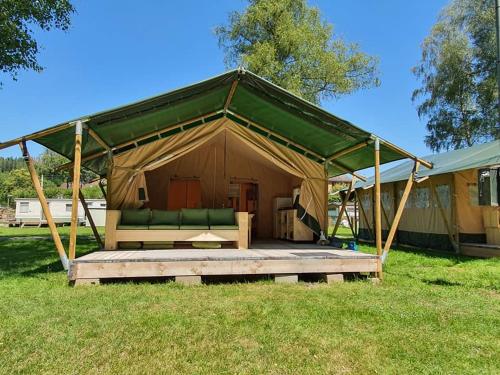 une tente avec un canapé vert dans un champ dans l'établissement Safaritent op Camping la Douane, à Vresse-sur-Semois