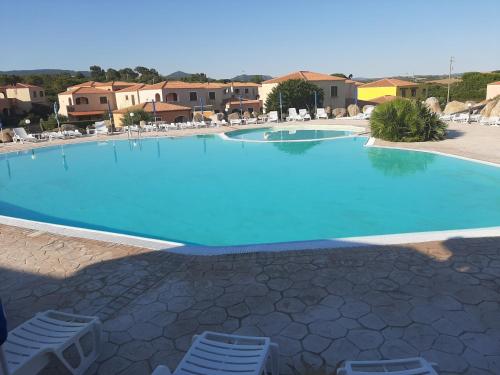 a large blue swimming pool with chairs and buildings at Appartamento Residence Mirice Vignola mare Aglientu casa Giorgia in Aglientu