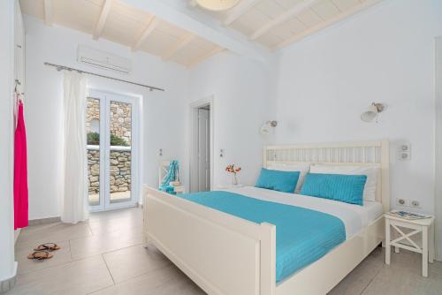 a white bedroom with a large bed with blue pillows at CORFOS BLUE MYKONOS in Ornos