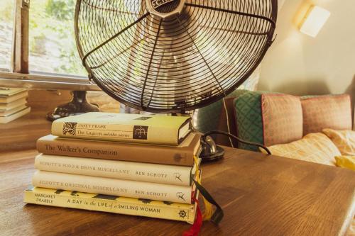 a stack of books sitting on a table with a fan at Dixie Airstream - Retro 1970s American Airstream close to Windermere in Staveley
