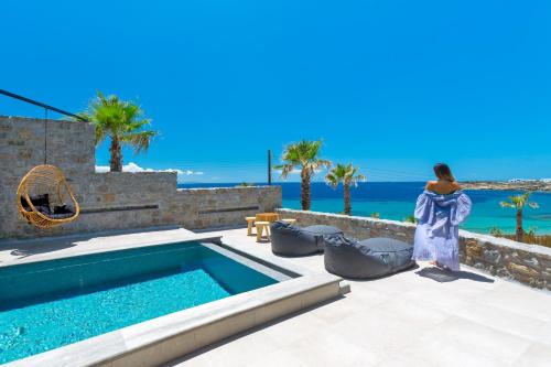 a woman is standing next to a swimming pool at Tropicana Hotel , Suites & Villas Mykonos in Paradise Beach