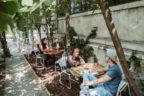 a group of people sitting at tables in a garden at Baroque Hostel & Coworking in Budapest