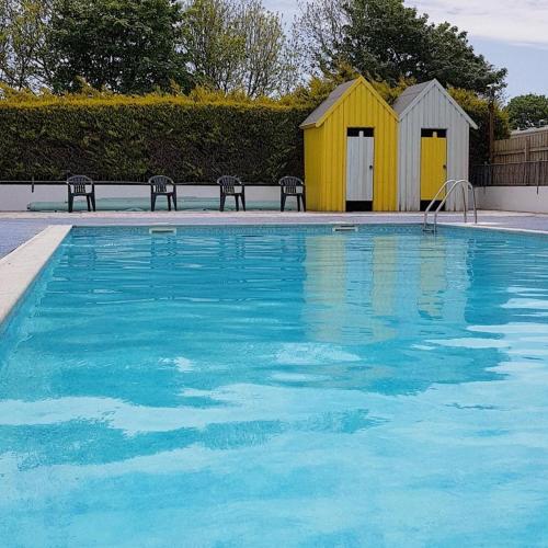 a swimming pool with a yellow building next to it at BRANWOOD Luxury Caravan Holidays Newquay in Newquay
