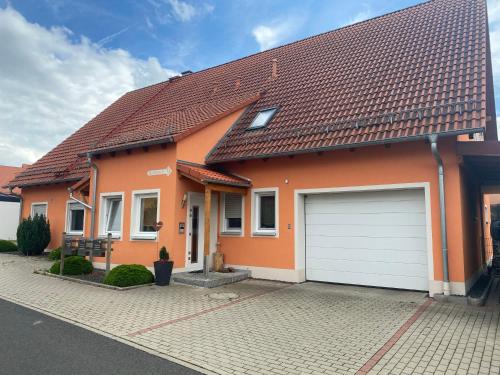 ein orangefarbenes Haus mit einer weißen Garage in der Unterkunft Steigerwaldblick Apartments Burgebrach in Burgebrach