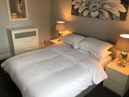 a large white bed in a bedroom with two lamps at The Station Apartment in Kilmarnock
