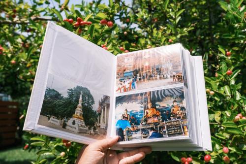 a person holding up two photographs in front of a tree at RiverTree House in Nong Khai