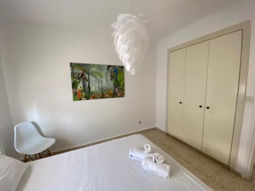 a white bedroom with a chair and a chandelier at Orphanides Latchi Apartment in Polis Chrysochous